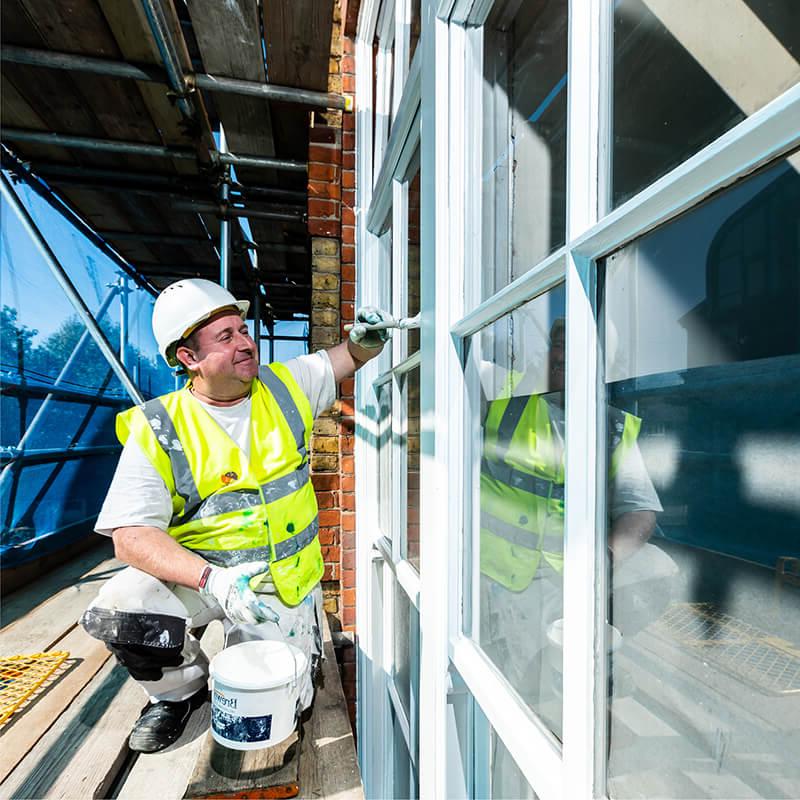 Mitie colleague painting a window frame